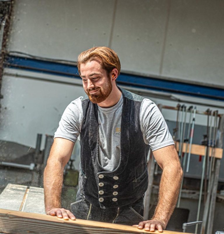 Handwerk mit Leidenschaft Elias Grabner schneidet lächelnd Holz an einer Tischkreissäge – authentische Energieberatung mit Praxisbezug.