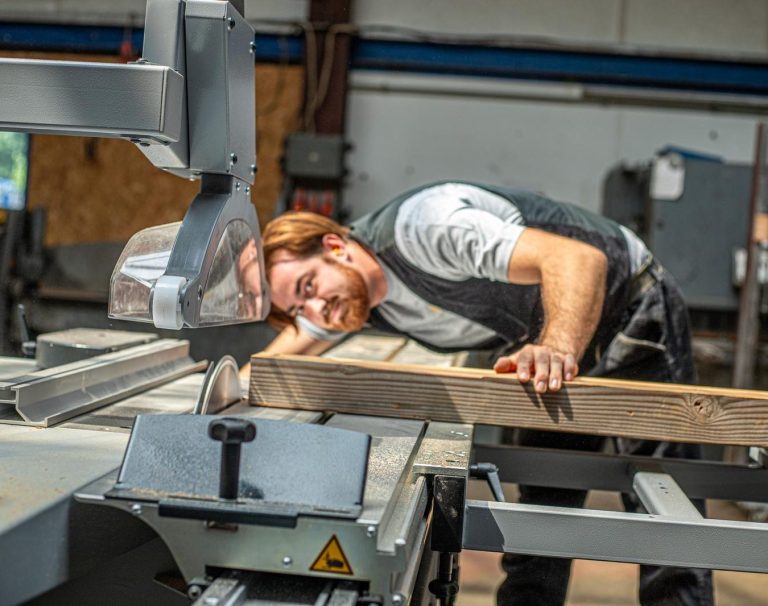 Handwerk mit Leidenschaft Elias Grabner schneidet lächelnd Holz an einer Tischkreissäge – authentische Energieberatung mit Praxisbezug.